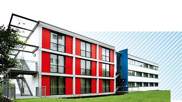 Das Gästehaus des Berufsförderwerks Koblenz: Dreistöckiges Neubaugebäude mit Außentreppen und roter Fassade.