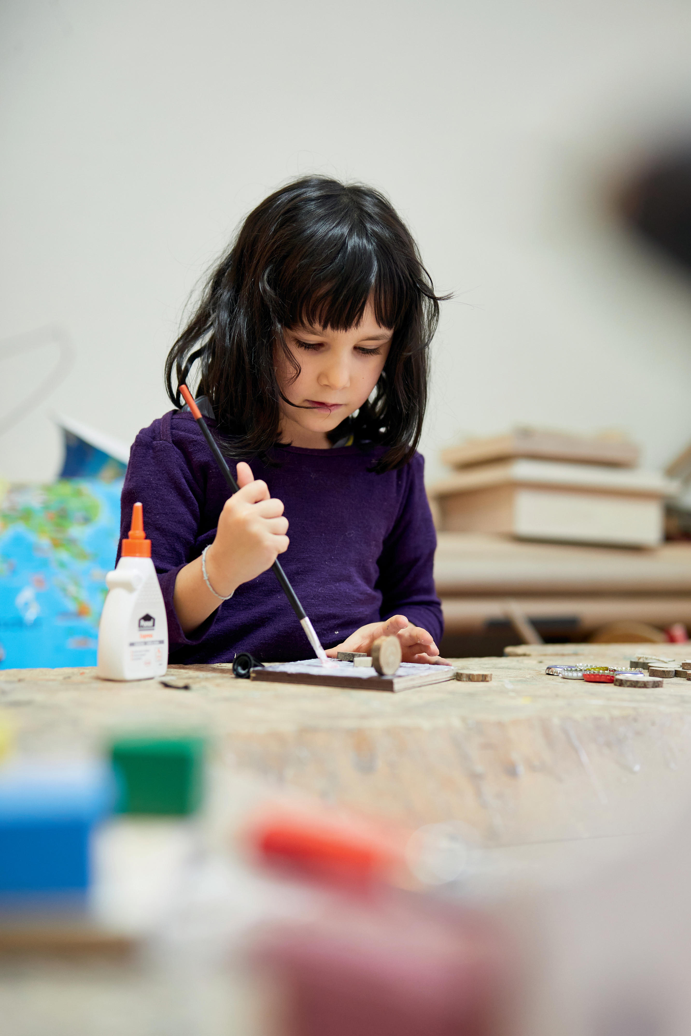 Ein kleines Mädchen malt mit einem Pinsel auf einer Holzplatte.