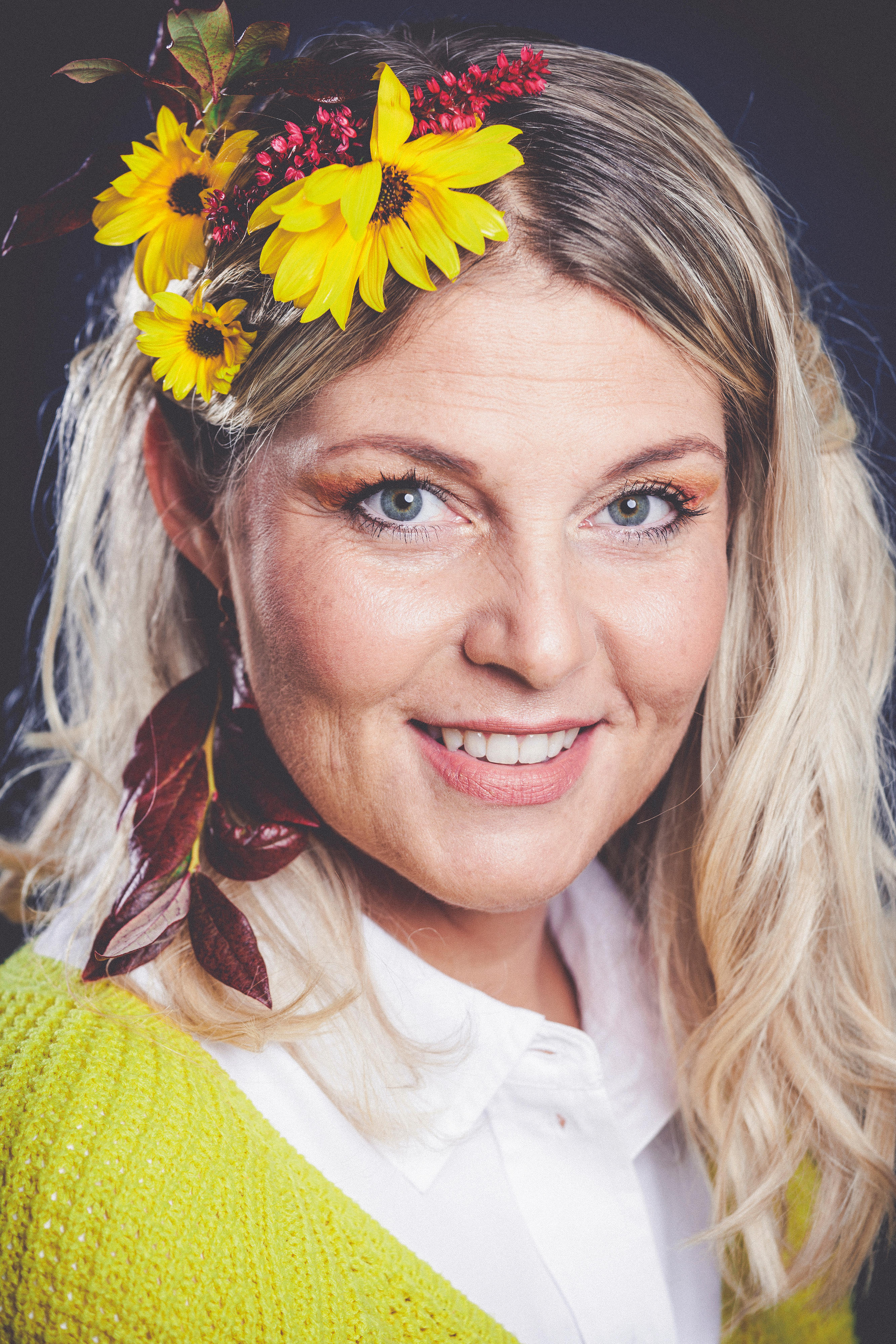 Porträt einer blonden, lächelnden Frau mit gelben und roten Blumen im Haar
