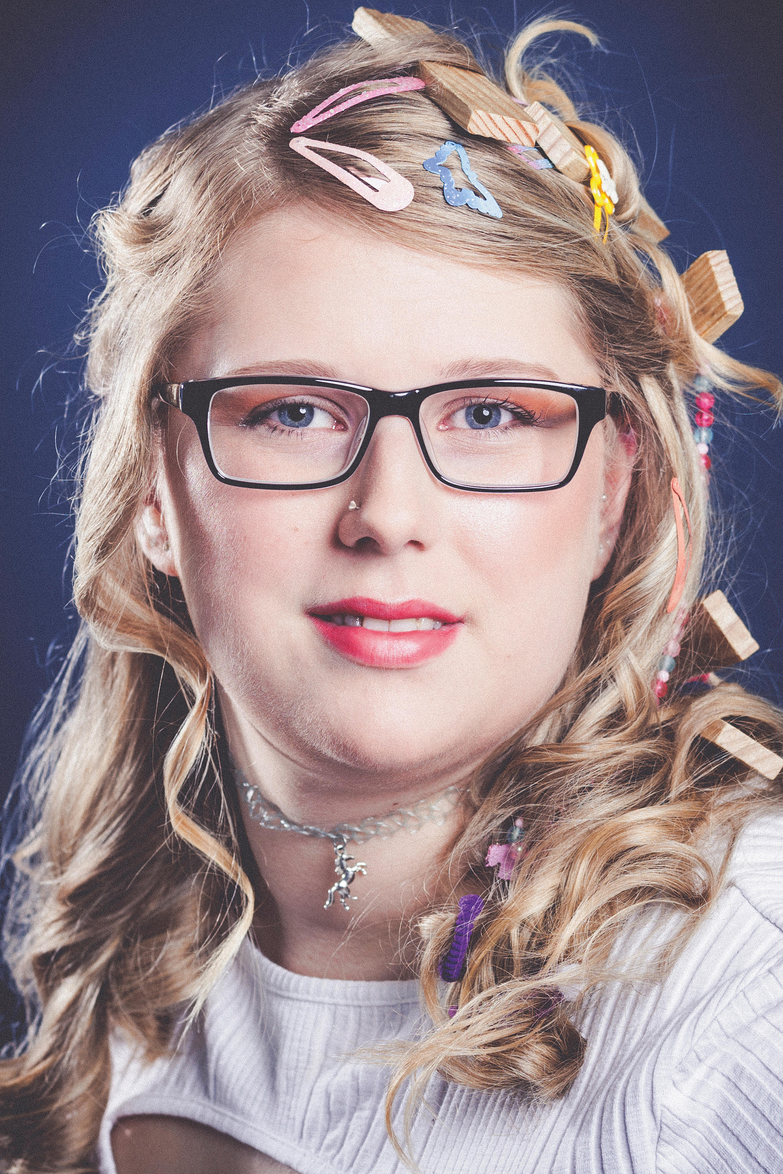Porträt einer blonden, lächelnden Frau mit Brille mit bunten Spangen und Holzscheiben im Haar