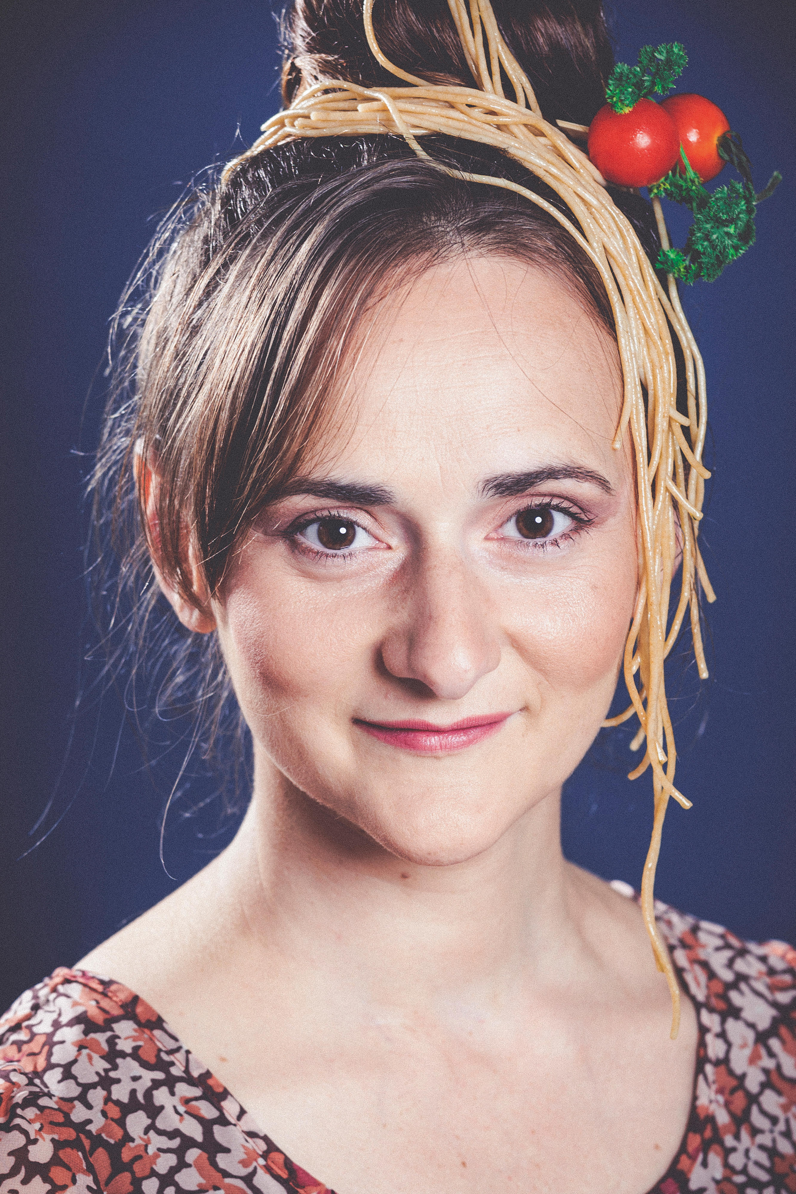 Porträt einer brünetten, lächelnden Frau mit Spaghetti und Tomaten im Haar