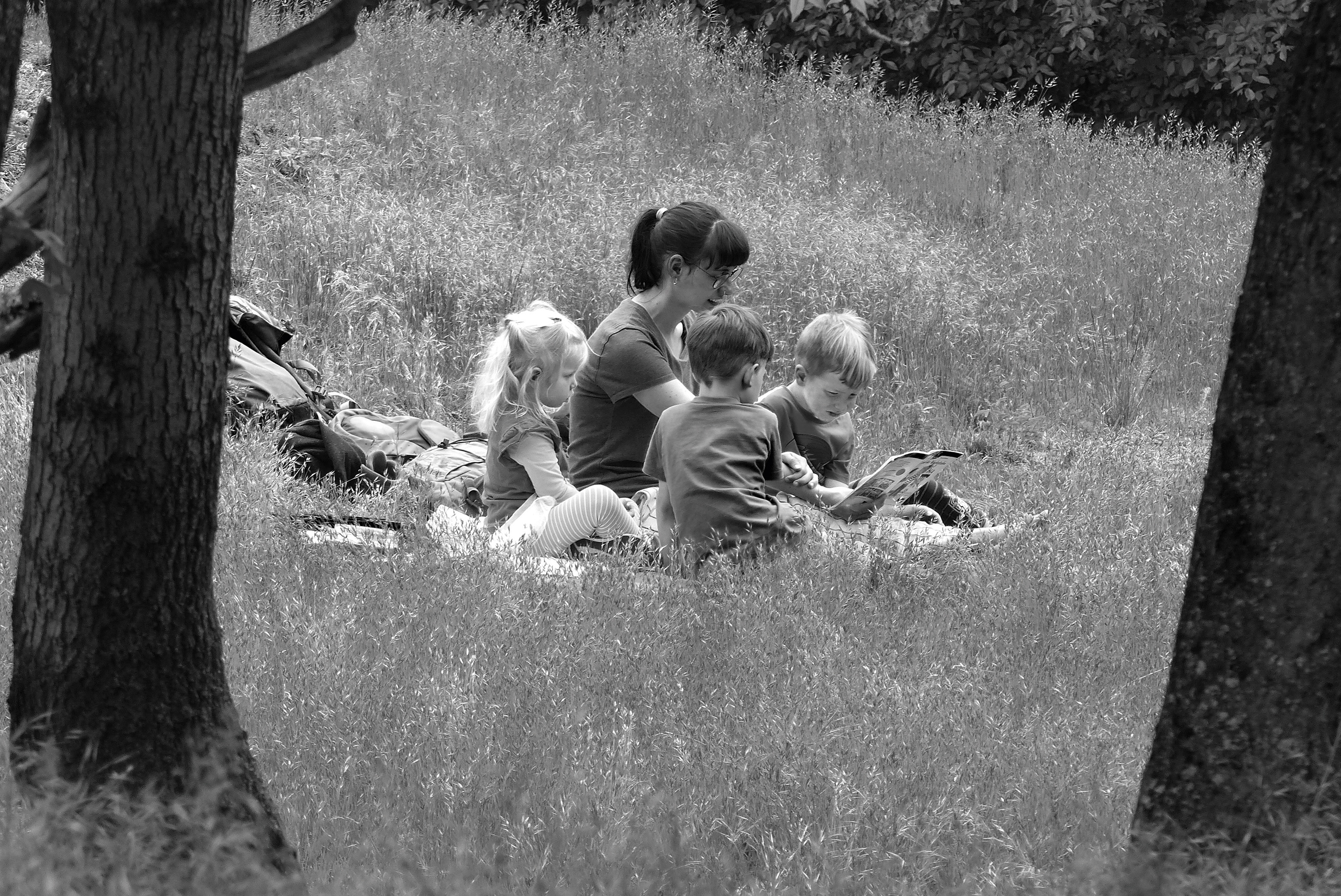 Schwarz-weiß-Aufnahme: Eine Frau sitzt mit drei Kindern auf einer Wiese.