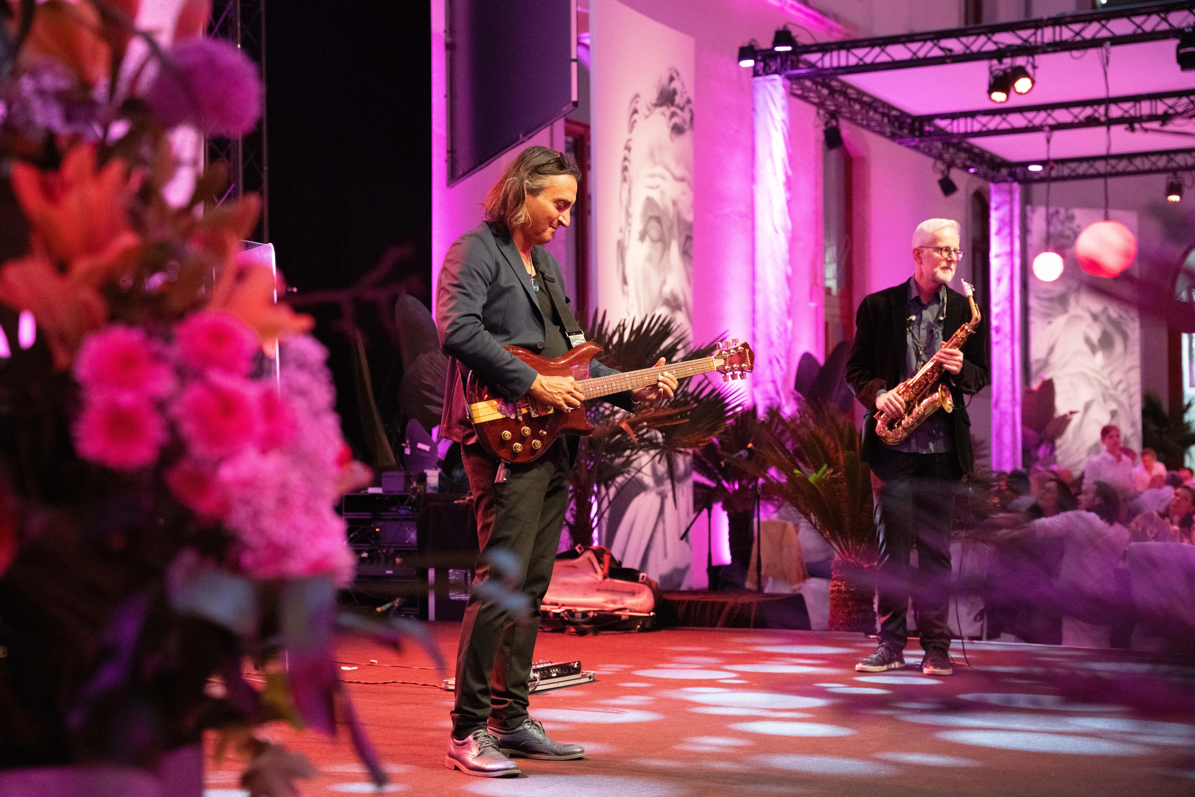 Zwei Musiker mit E-Gitarre und Saxofon in einem festlich beleuchteten Bühnenbereich