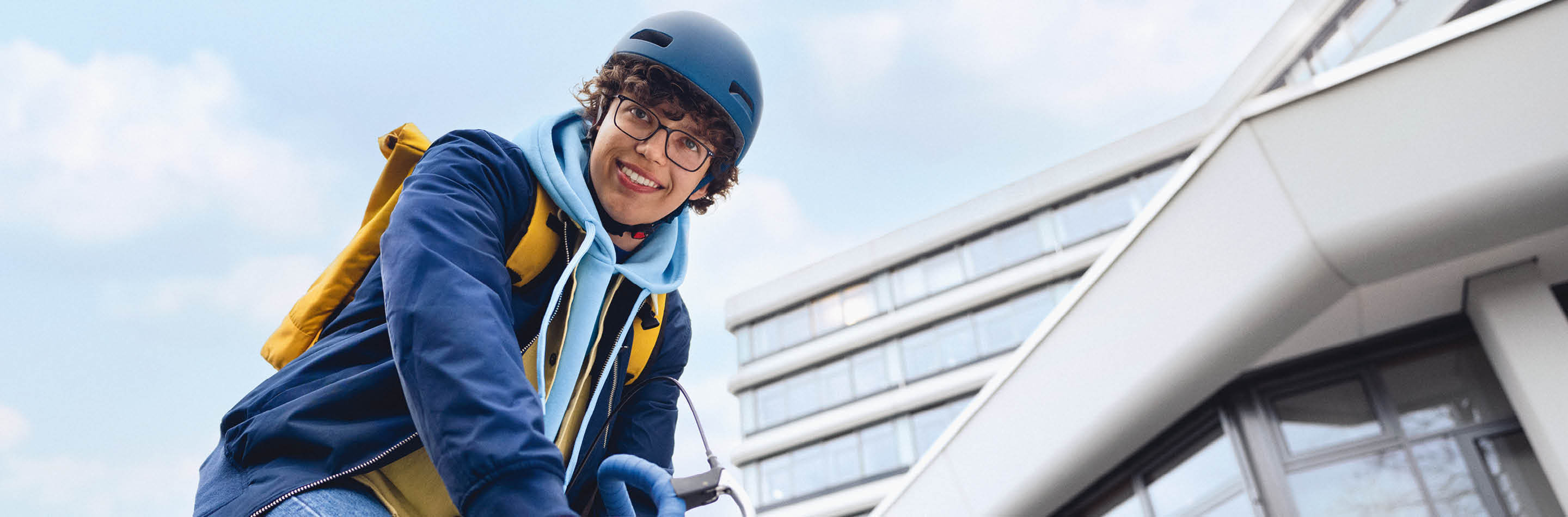 1000 UNDEIN GRUND – Deine Idee von Karriere: mehr bewirken. Ein junger Mann sitzt lächelnd auf einem Fahrrad.