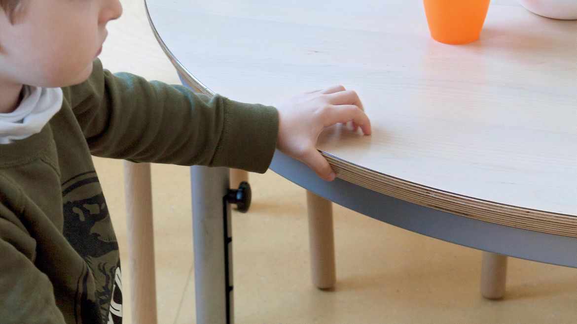 Ein kleiner Junge sitzt auf einem Kinderstuhl an einem Tisch.