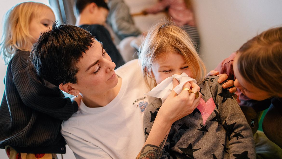 Eine Frau putzt einem kleinen Mädchen mit einem Papiertaschentuch die Nase