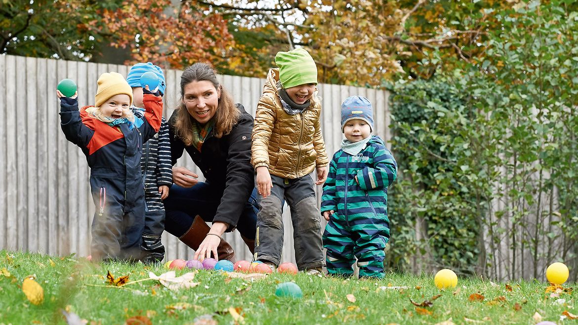 Eine Frau spielt mit vier Kindern auf dem Rasen. Alle tragen Winterkleidung.