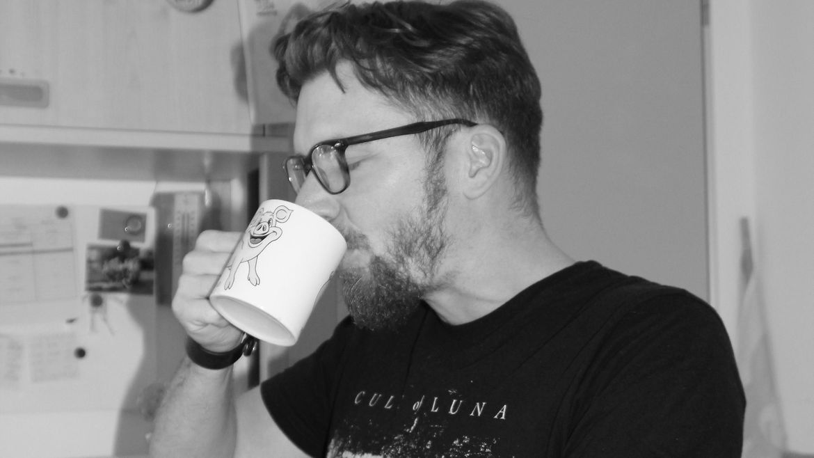 Schwarz-Weiß-Aufnahme: Ein Mann mit Bart und Brille trinkt mit geschlossenen Augen aus einer Kaffeetasse.