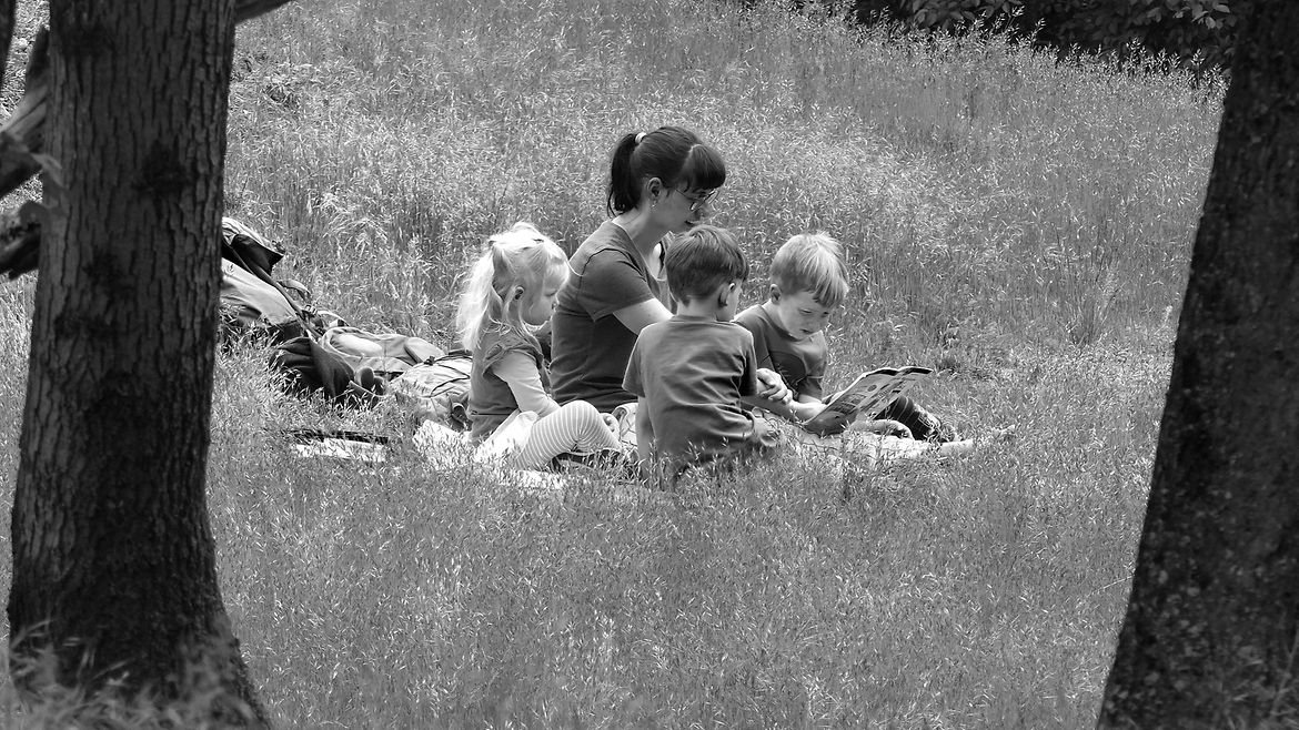 Schwarz-weiß-Aufnahme: Eine Frau sitzt mit drei Kindern auf einer Wiese.