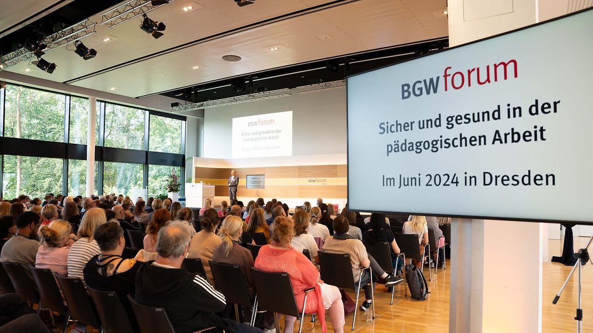Saalansicht mit sitzendem Publikum. Auf Monitoren steht "BGW forum Sicher und gesund in der pädagogischen Arbeit Im Juni 2024 in Dresden".