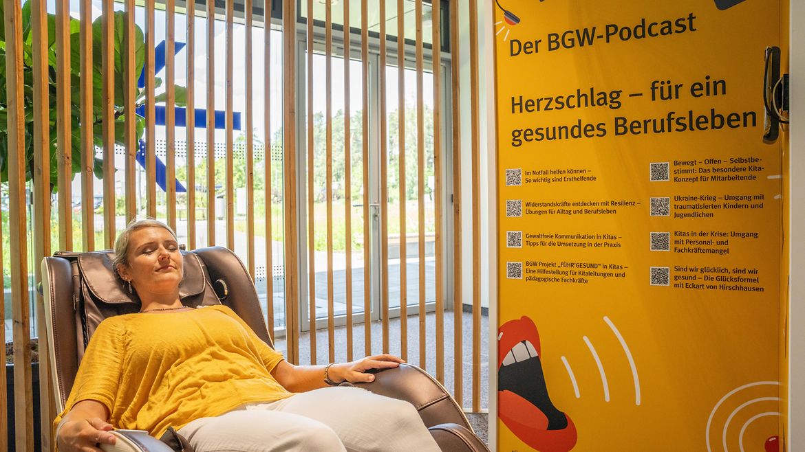 Eine Frau liegt mit geschlossenen Augen in einem Liegesessel, daneben Plakatwand unter anderem mit Text "Der BGW-Podcast. Herzschlag - für ein gesundes Berufsleben"