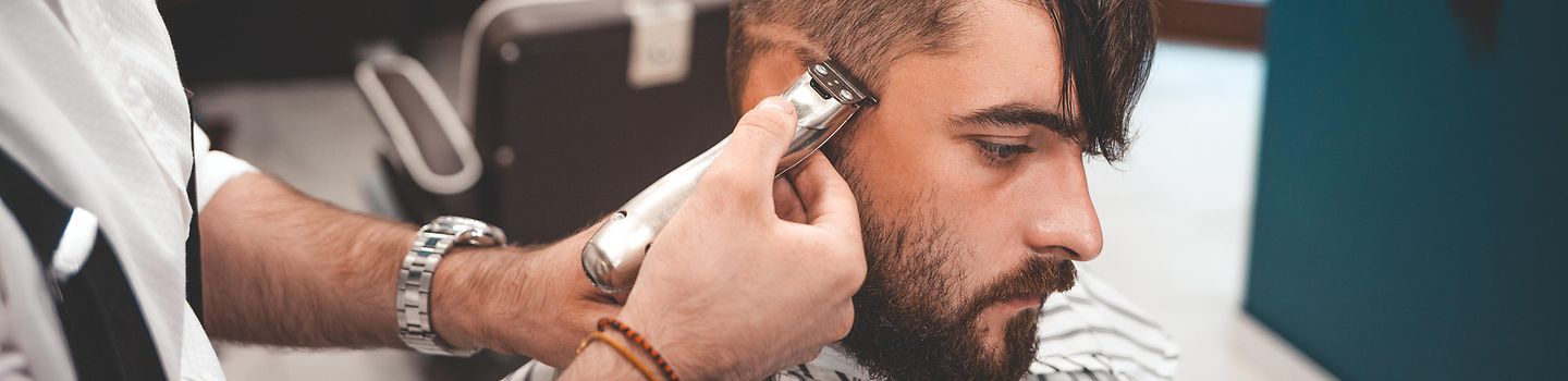 Friseur rasiert Kundenfrisur Ein Friseur rasiert am Kopf eines Kunden eine Linie.